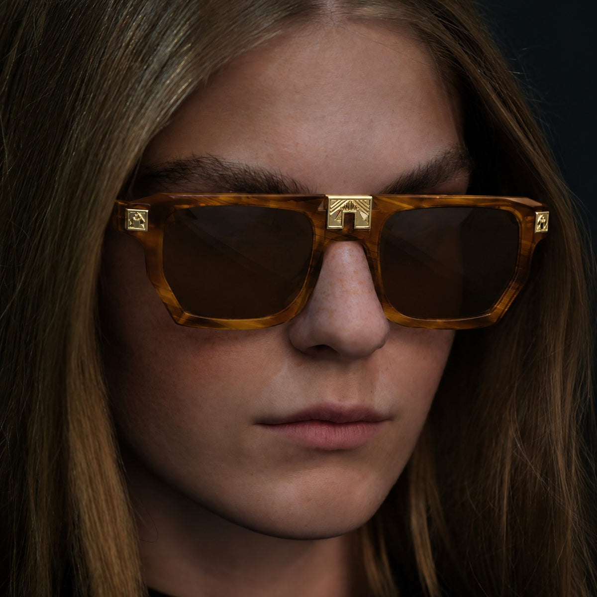 Model wearing ARIA NOIR ARCA II sunglasses in Caramel Stripe honey amber striped acetate with gold bridge detail